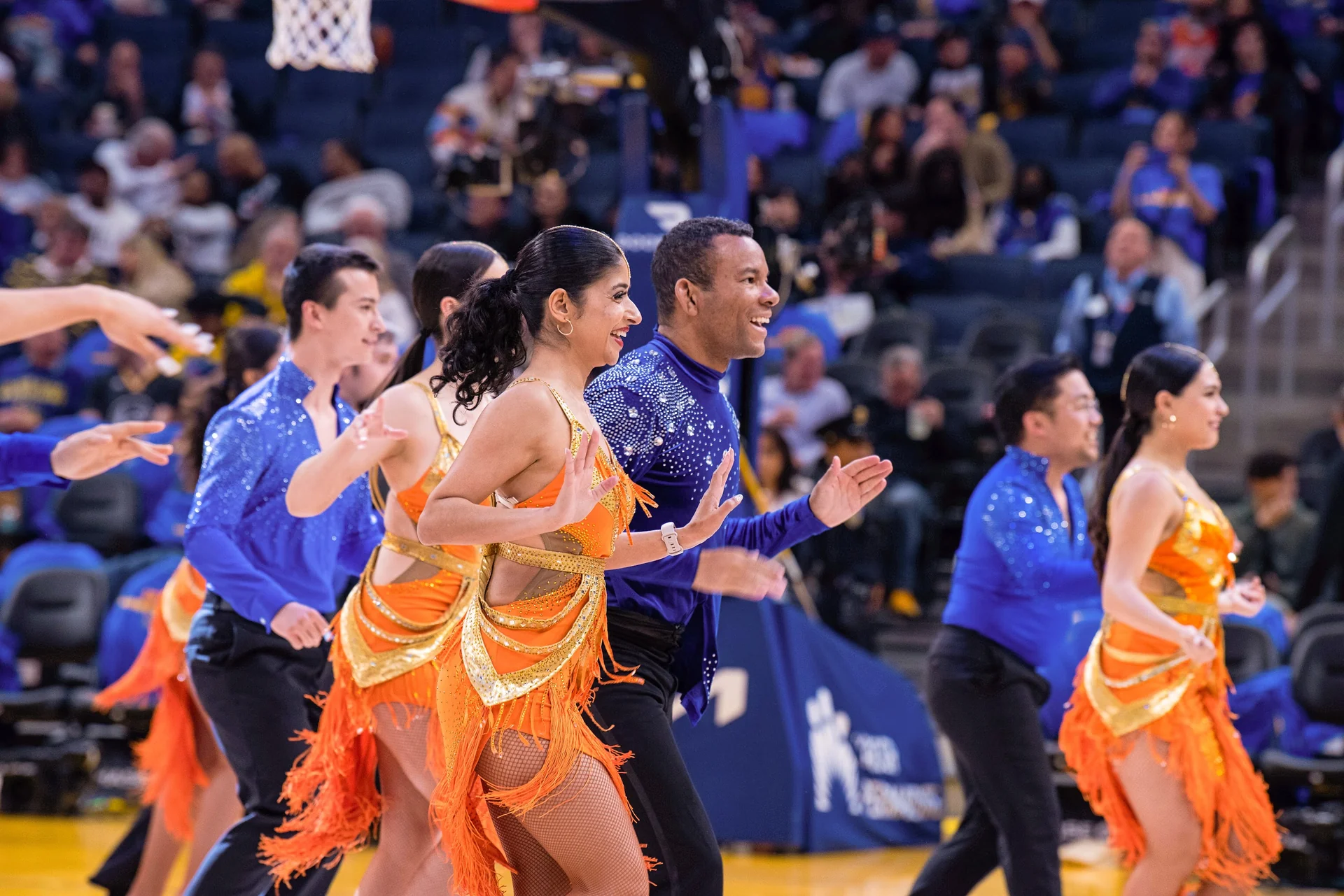 Takeshi Young and a salsa team performing in orange and blue costumes on a basketball court